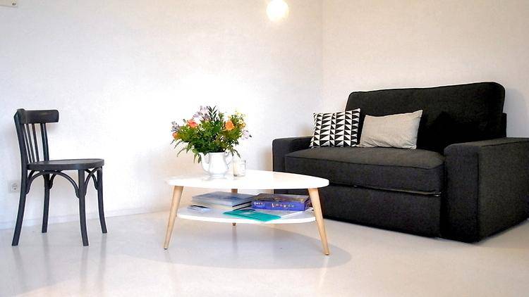 Minimalistisches Wohnzimmer mit dunklem Sofa, weißem Couchtisch und heller Einrichtung.