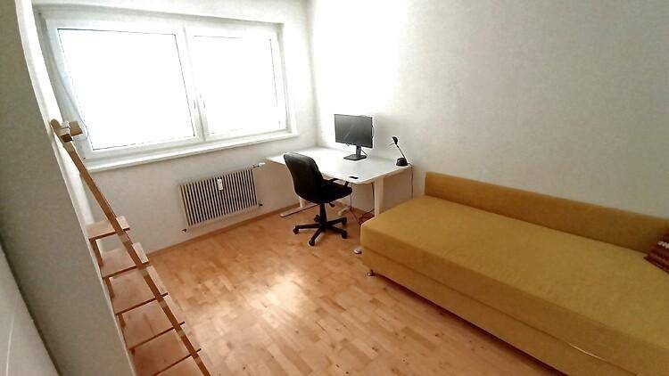 Helles Arbeitszimmer mit Schreibtisch, Bürostuhl und gelbem Tagesbett.