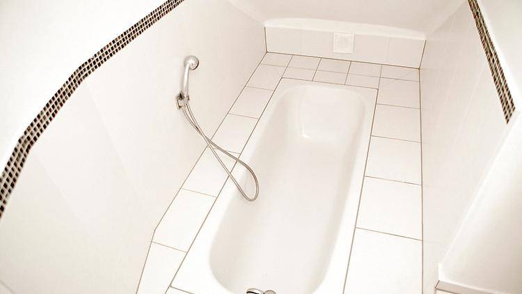 Weiß gefliestes Badezimmer mit einer Badewanne und einer praktischen Handbrause, sauber und hell.