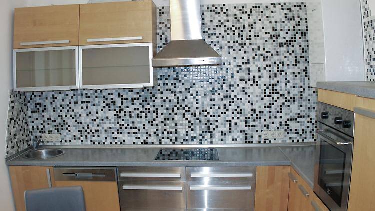 Moderne Küche mit Holzschränken, Induktionskochfeld, Geschirrspüler und einer auffälligen Mosaik-Rückwand.