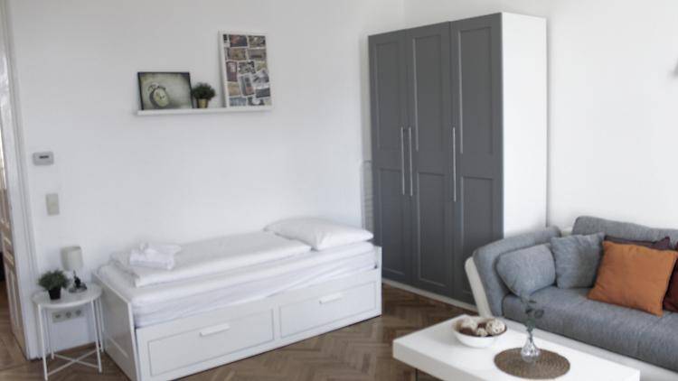 Multifunktionaler Raum mit Einzelbett, grauem Kleiderschrank und Sofa, ideal als Gäste- oder Wohnbereich.