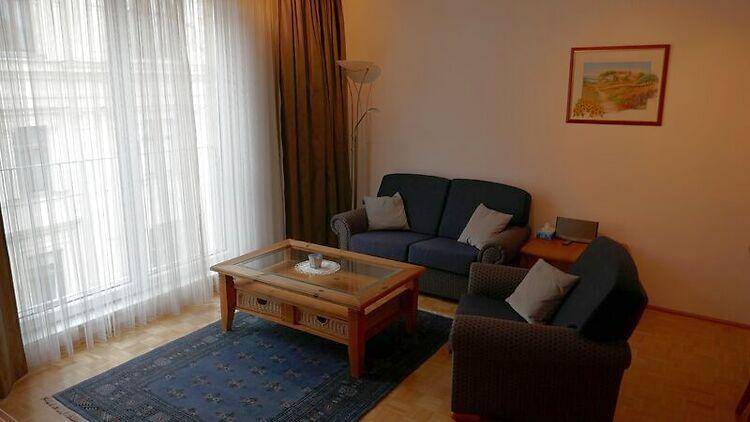 Gemütliches Wohnzimmer mit Sofa, Couchtisch und großen Fenstern mit Vorhängen.