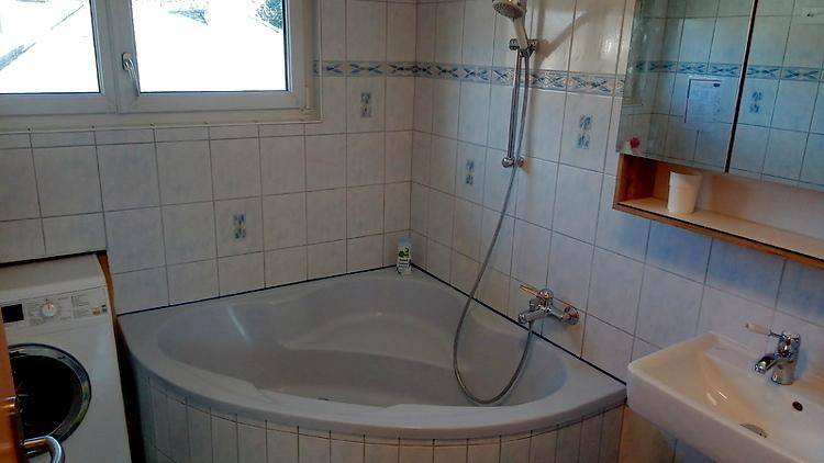 Badezimmer mit Eckbadewanne, Waschbecken, Fliesenwänden und Waschmaschine.