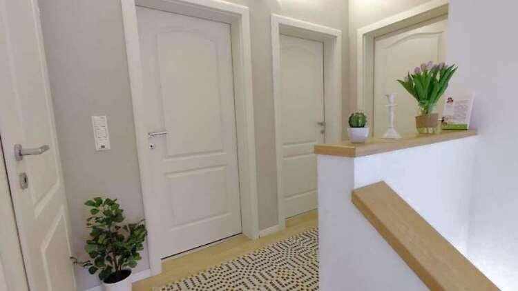 Heller Flur im Obergeschoss mit mehreren Türen und einer Holztreppe, dekoriert mit frischen Blumen.