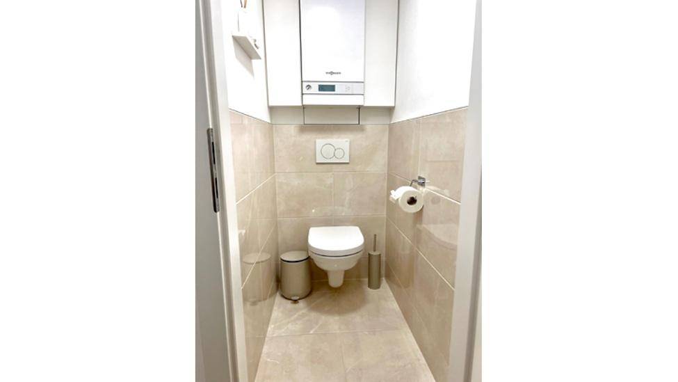 Separates WC mit wandhängender Toilette, Spülkasten und Heizungsanlage an der Wand.