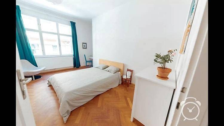 Helles Schlafzimmer mit Doppelbett, weißen Möbeln und großen Fenstern mit blauen Vorhängen.