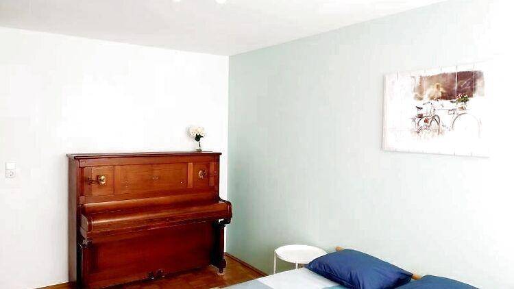 Schlafzimmer mit einem klassischen Klavier und einer dezent farbigen Wand, die Ruhe ausstrahlt.