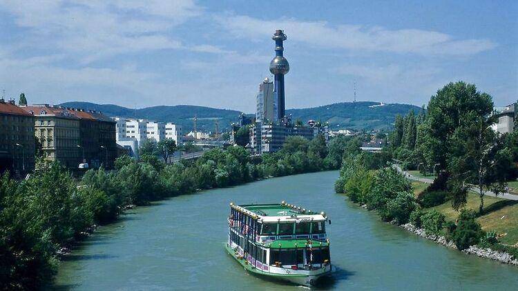 Panoramablick auf den Fluss mit einem Boot, umgeben von Bäumen und Stadtgebäuden.