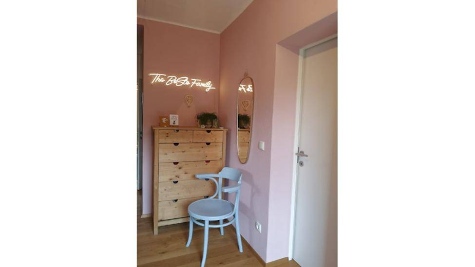 Flur mit rosa Wänden, einer Holzkommode, einem Spiegel und einem dekorativen Neonlicht.