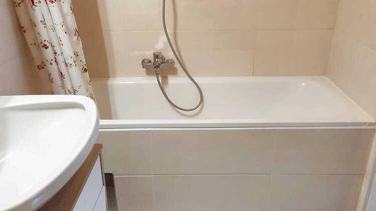 Badezimmer mit Badewanne, Duschvorhang und Waschbecken, hell gefliest.