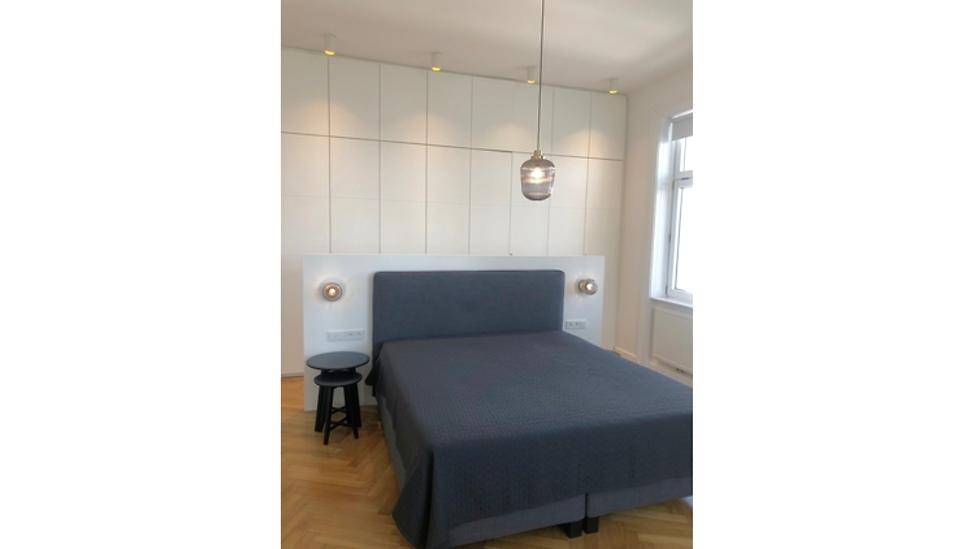 Schlafzimmer mit Doppelbett, integrierten Schränken und Parkettboden, beleuchtet von einer Hängelampe.