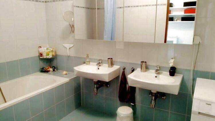 Badezimmer mit Badewanne, Doppelwaschbecken und hellblauen Fliesen, ausgestattet mit Spiegelschrank.