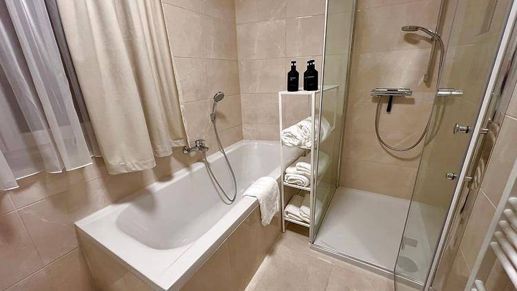 Modernes Badezimmer mit Badewanne, Duschkabine, beigefarbenen Fliesen und Handtuchheizkörper.