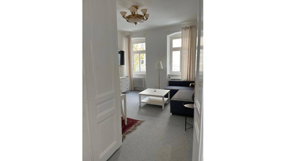 Blick in ein helles Wohnzimmer mit Sofa, Couchtisch und großen Fenstern, die viel Licht spenden.