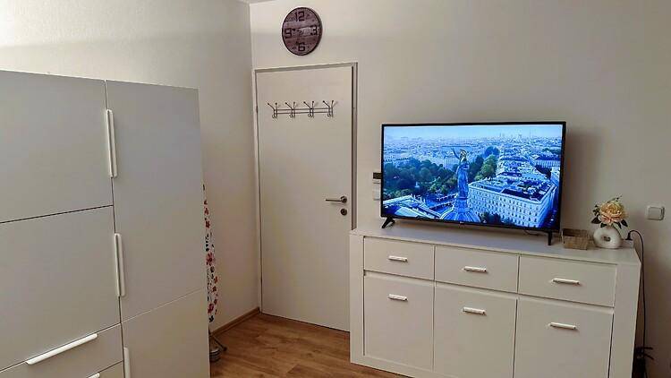 Wand mit Fernseher auf einer Kommode und einer Tür mit Garderobenhaken.