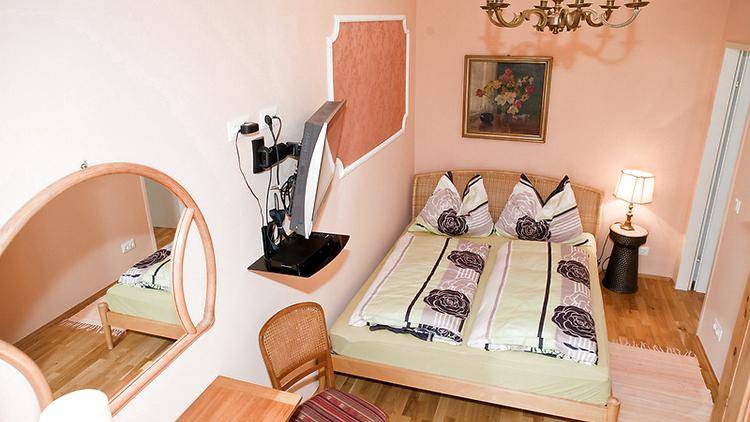 Gemütliches Schlafzimmer mit Doppelbett, Holzboden und pastellfarbenen Wänden, ausgestattet mit einem Fernseher.
