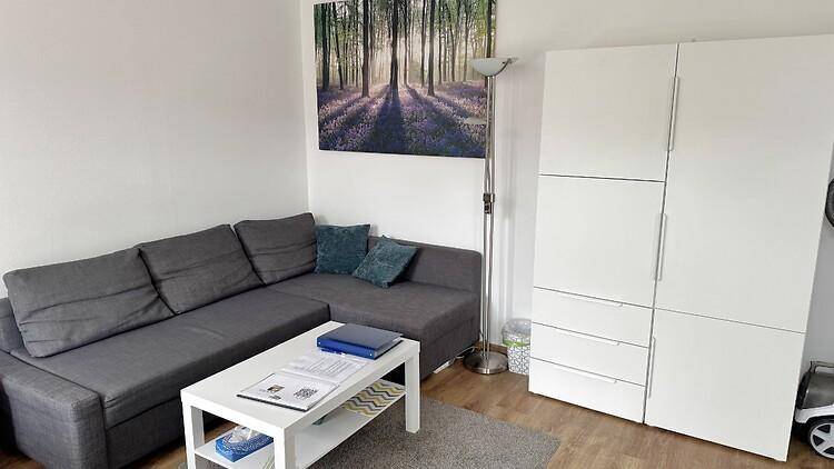 Gemütlicher Wohnbereich mit Ecksofa, Couchtisch und praktischem weißen Kleiderschrank.