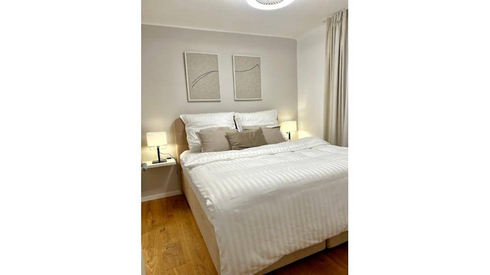 Helles Schlafzimmer mit Doppelbett, Nachttischen und Holzboden, ausgestattet mit moderner Dekoration.