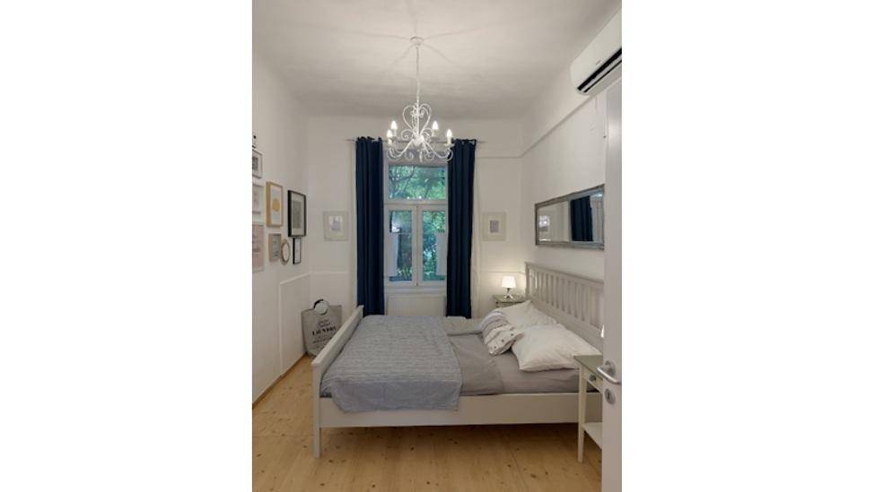 Helles Schlafzimmer mit Doppelbett, Kronleuchter und Klimaanlage in einem hohen Raum.