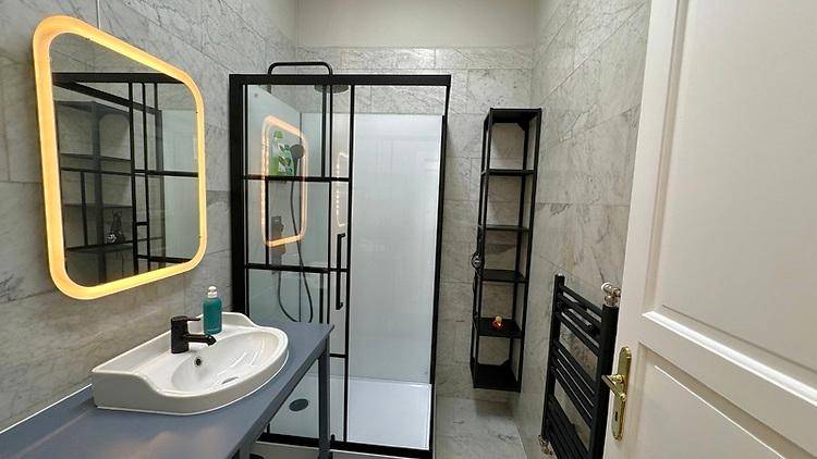 Modernes Badezimmer mit begehbarer Dusche, beleuchtetem Spiegel und grauen Marmorfliesen.