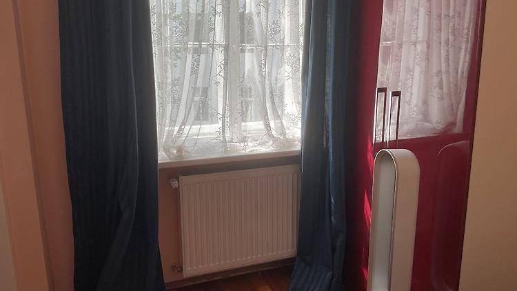 Fenster mit Vorhängen, Heizkörper und modernem Ventilator in einem hellen Raum.