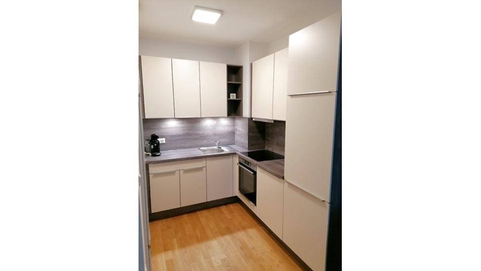 Moderne Einbauküche in hellen Farbtönen mit integrierten Geräten und Holzboden.