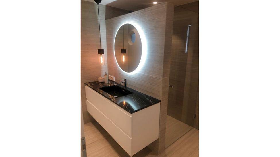 Modernes Badezimmer mit beleuchtetem Spiegel, Waschtisch mit dunkler Platte und begehbarer Dusche.