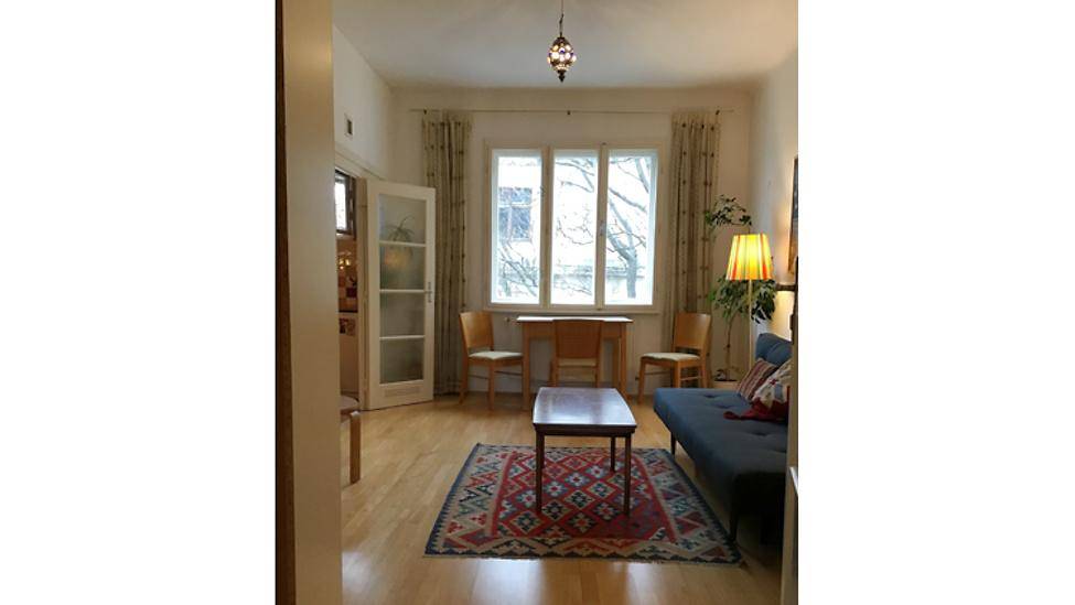 Geräumiges Wohnzimmer mit Holzboden, großem Fenster und einem kleinen Esstischbereich.