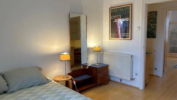 Schlafzimmer mit Bett, Nachttisch, Stehspiegel und einem Heizkörper unter einem Poster.