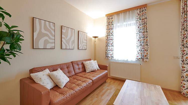 Gemütliches Wohnzimmer mit beiger Wandfarbe, braunem Ledersofa und hellem Laminatboden.