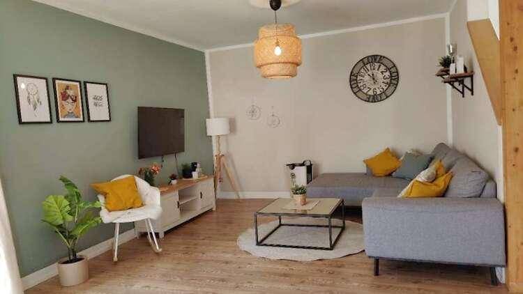 Gemütliches Wohnzimmer mit hellem Holzboden, bequemer Couch und moderner Dekoration in Grüntönen.