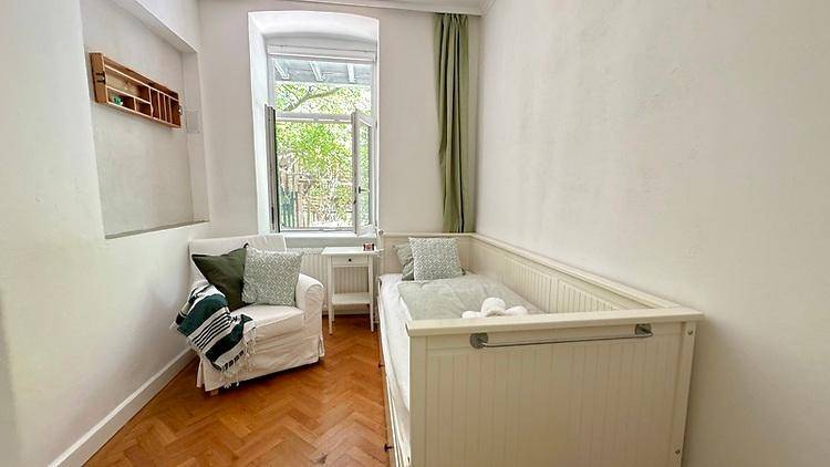 Helles Zimmer mit Babybett, Sessel und Fenster mit Blick ins Grüne.