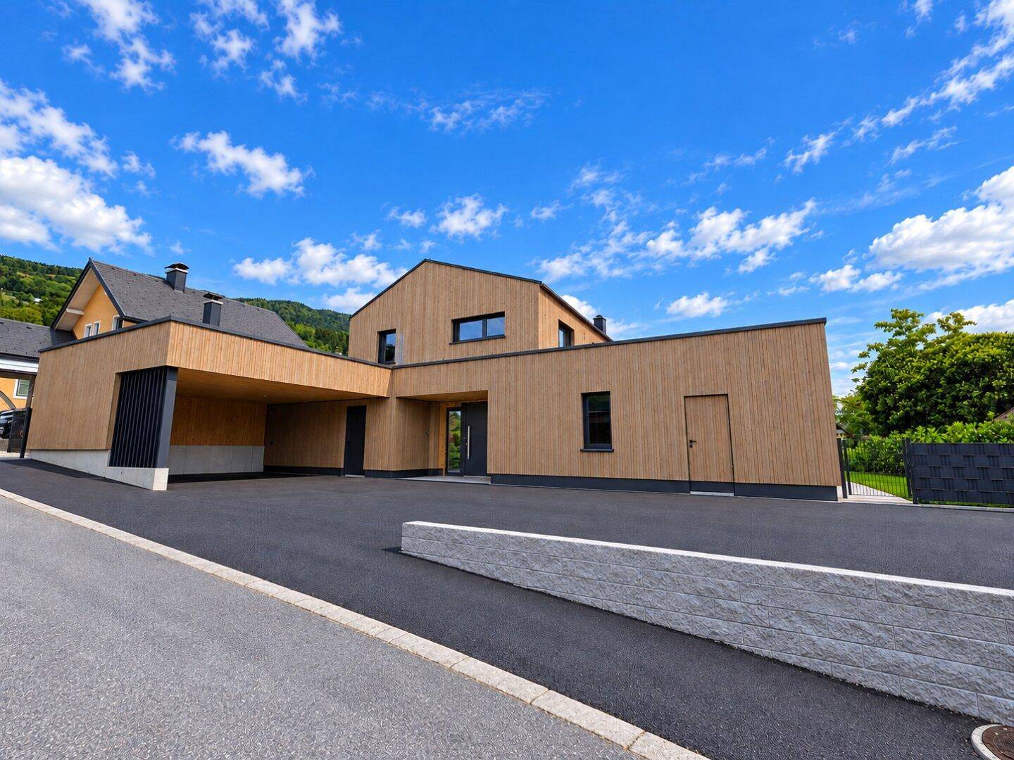 Modernes Einfamilienhaus mit Holzfassade, Carport und gepflegter Auffahrt.