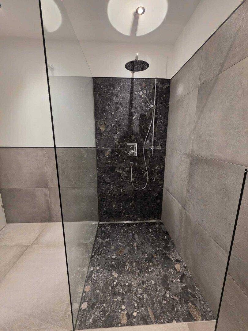 Geräumige begehbare Dusche mit Regenduschkopf und dunklen, großformatigen Fliesen.