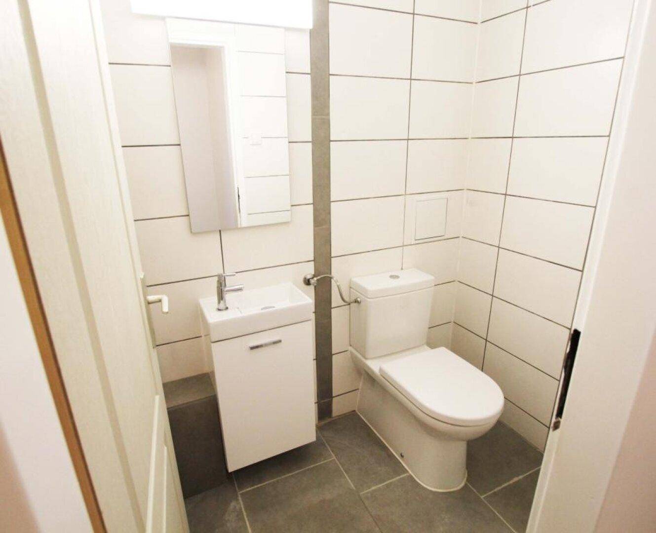 Modernes Gäste-WC mit weißen Wandfliesen, Hänge-WC und kleinem Waschbecken.