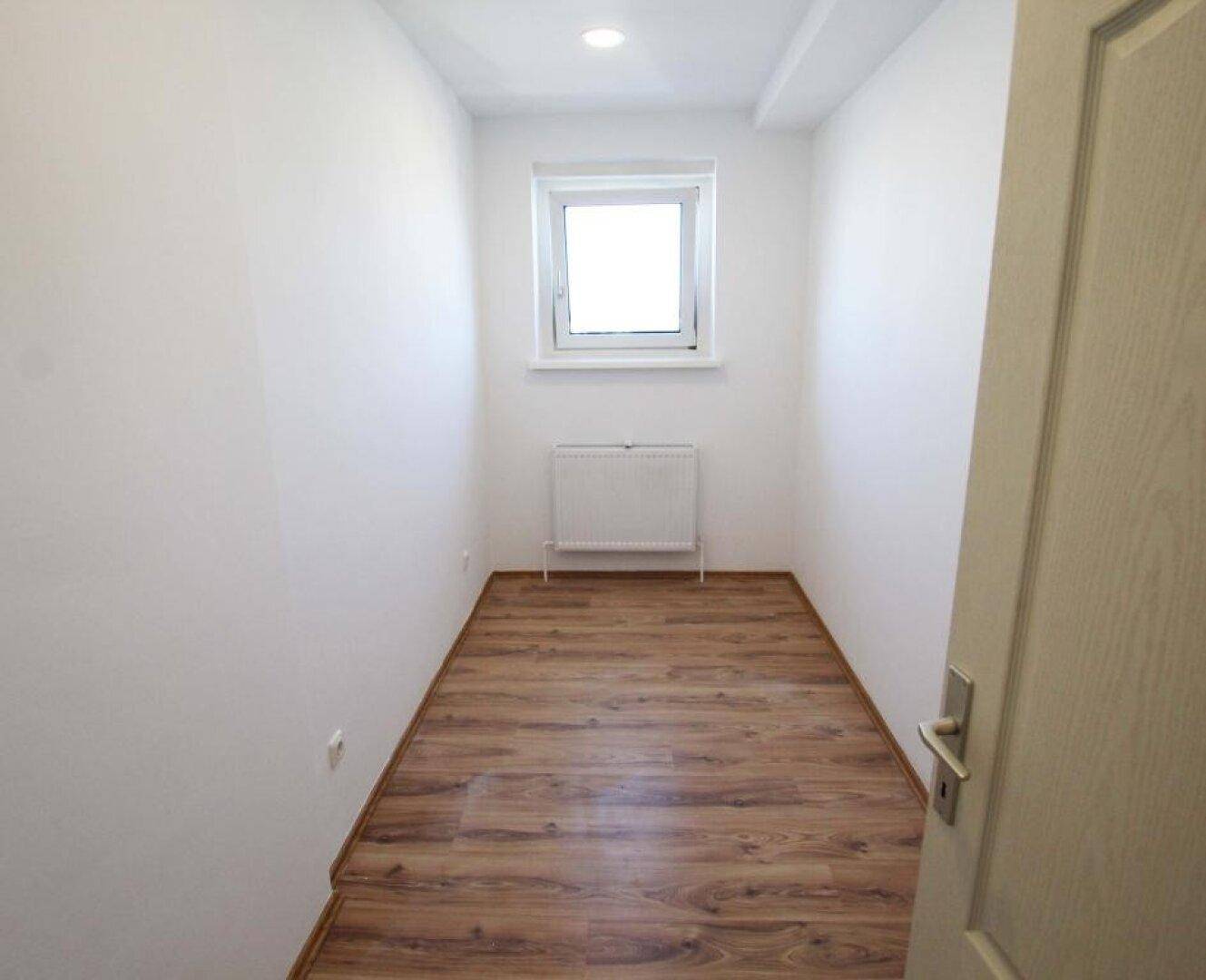 Kleiner, heller Raum mit Laminatboden und einem Fenster, ideal als Abstellraum oder Büro.