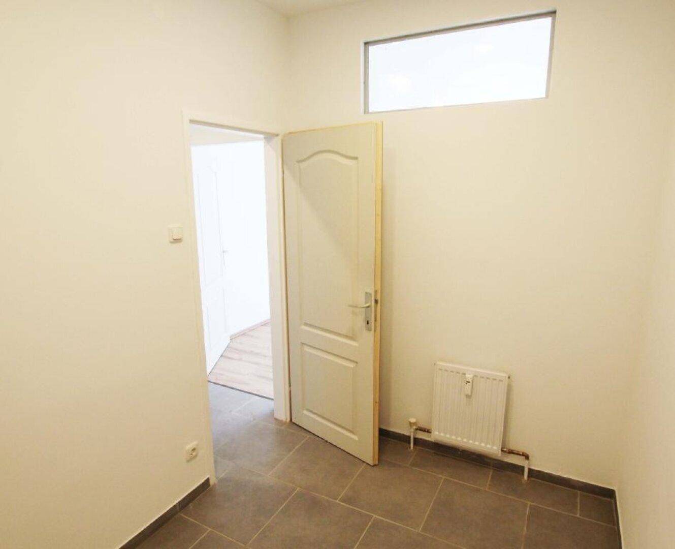 Kleiner Raum mit Fliesenboden und einem hohen Fenster, ideal als Abstell- oder Hauswirtschaftsraum.