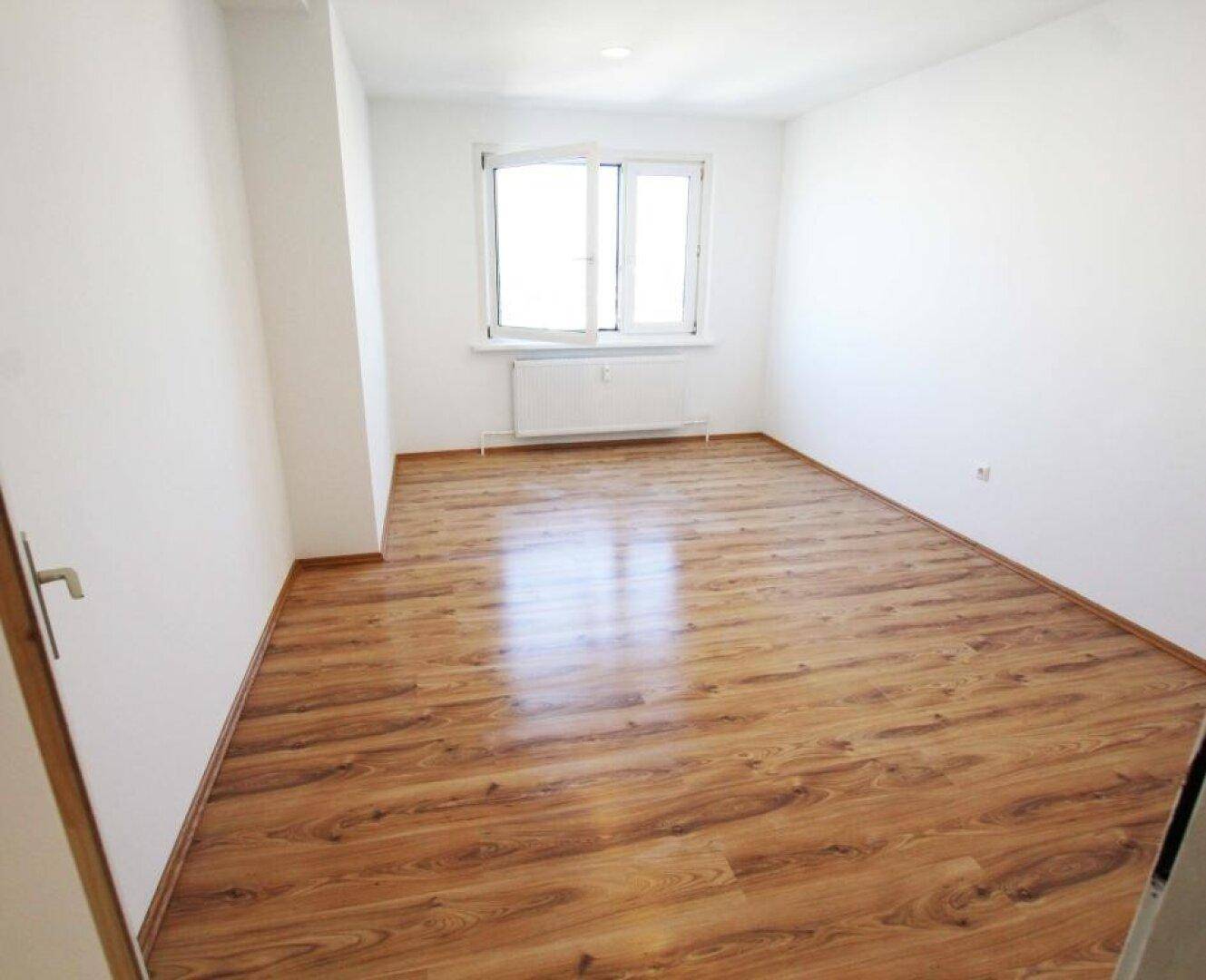 Geräumiges, helles Zimmer mit Laminatboden und großem Fenster, bereit zur individuellen Gestaltung.