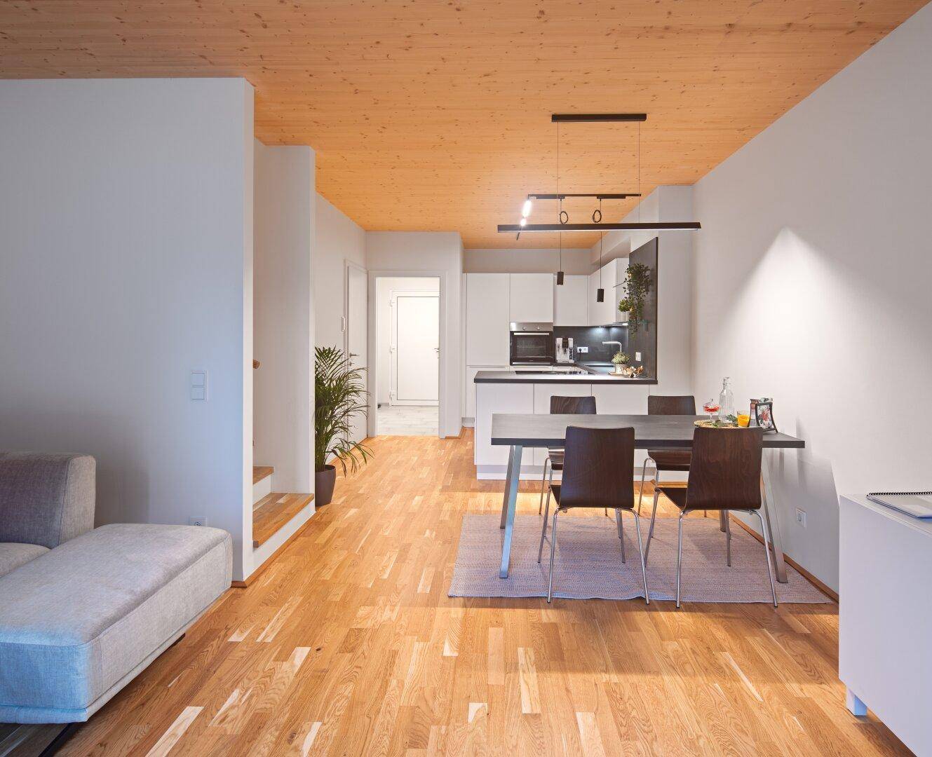 Geräumiger Wohn- und Essbereich mit Holzboden, der in eine moderne Küche übergeht.