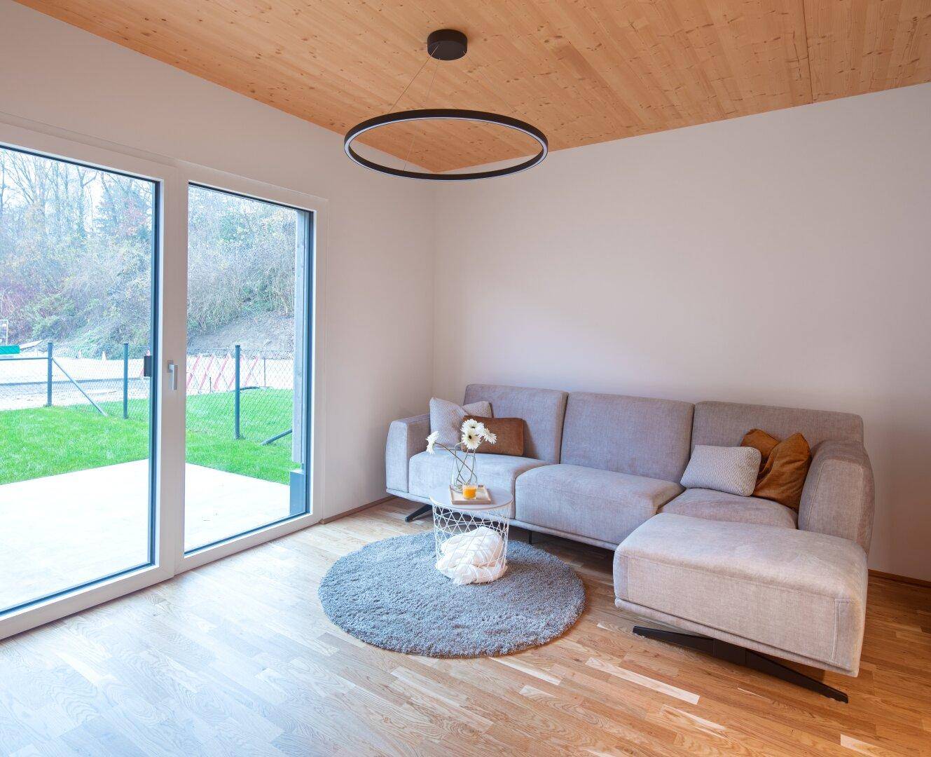 Gemütlicher Wohnbereich mit Sofa, runder Teppich und großen Fenstern zum Garten.