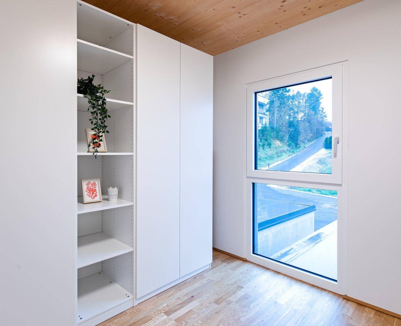 Helles Schlafzimmer mit Holzboden, weißen Einbauschränken und Fenster mit Ausblick.