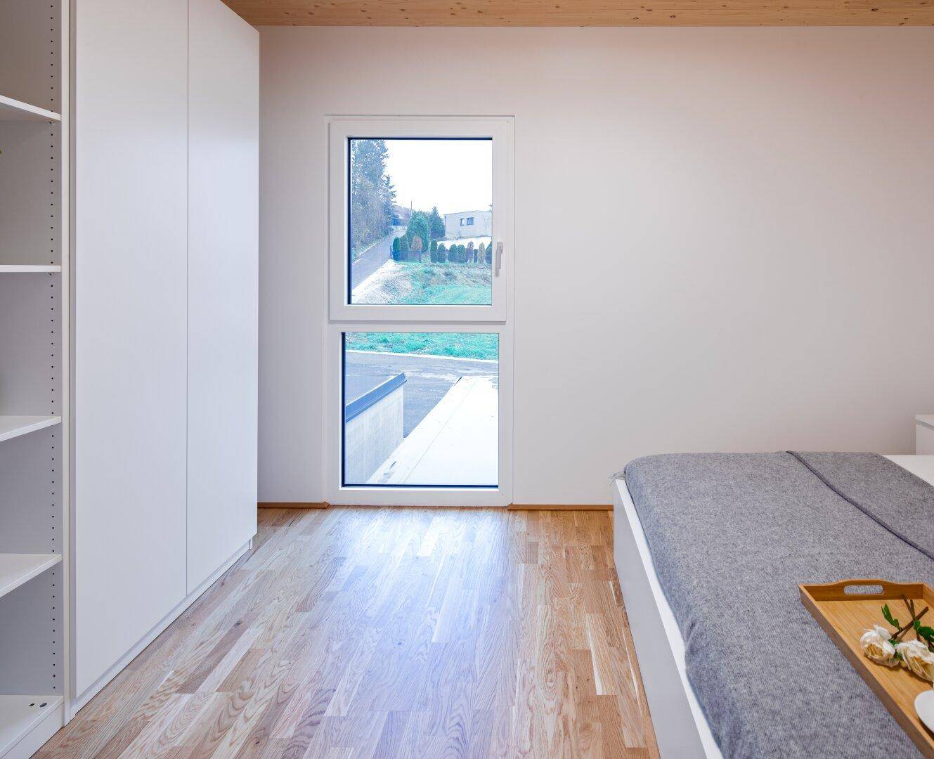 Schlafzimmer mit Holzboden, weißen Einbauschränken und Fenster mit Blick nach draußen.