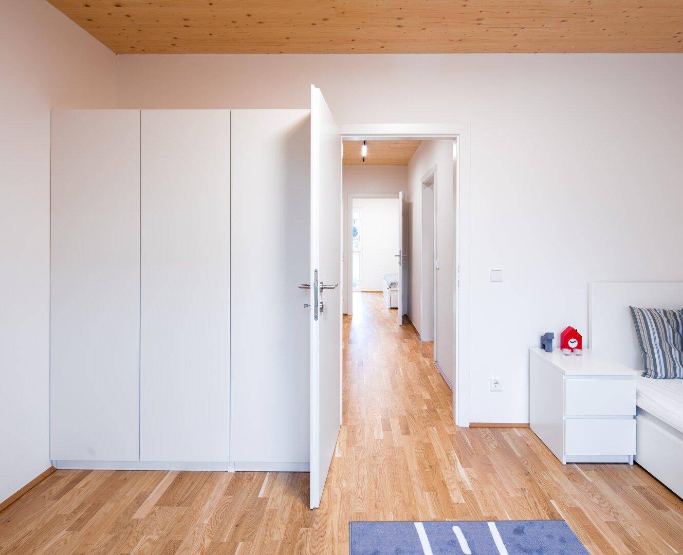 Schlafzimmer mit Holzboden, weißen Einbauschränken und Zugang zum Flur.