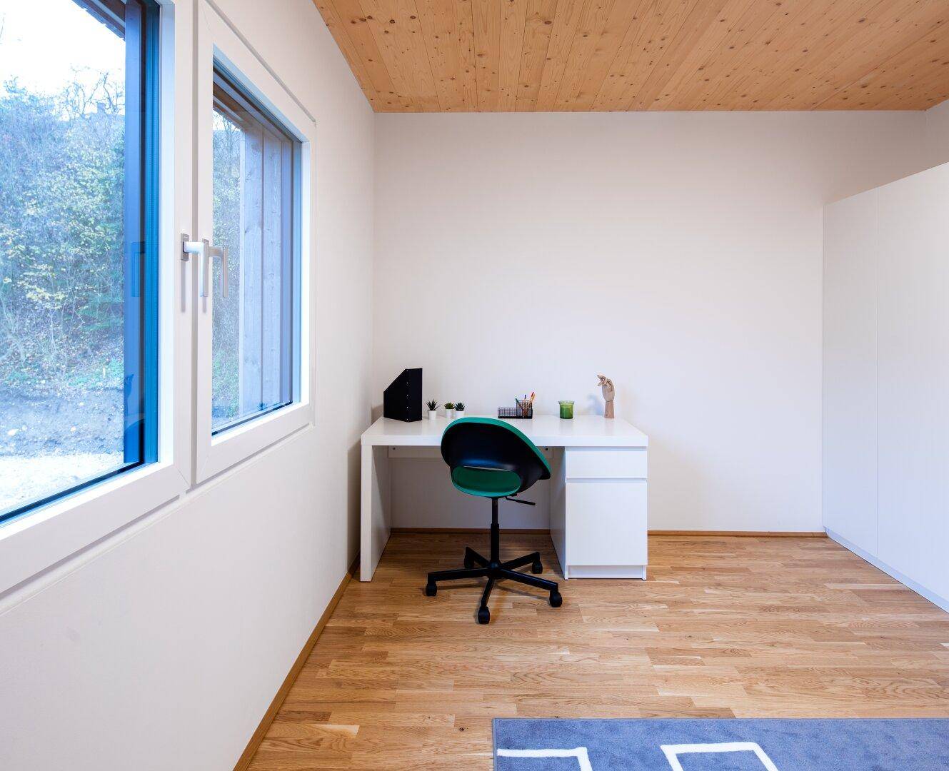 Helles Arbeitszimmer mit Holzboden, weißem Schreibtisch und Blick ins Grüne.
