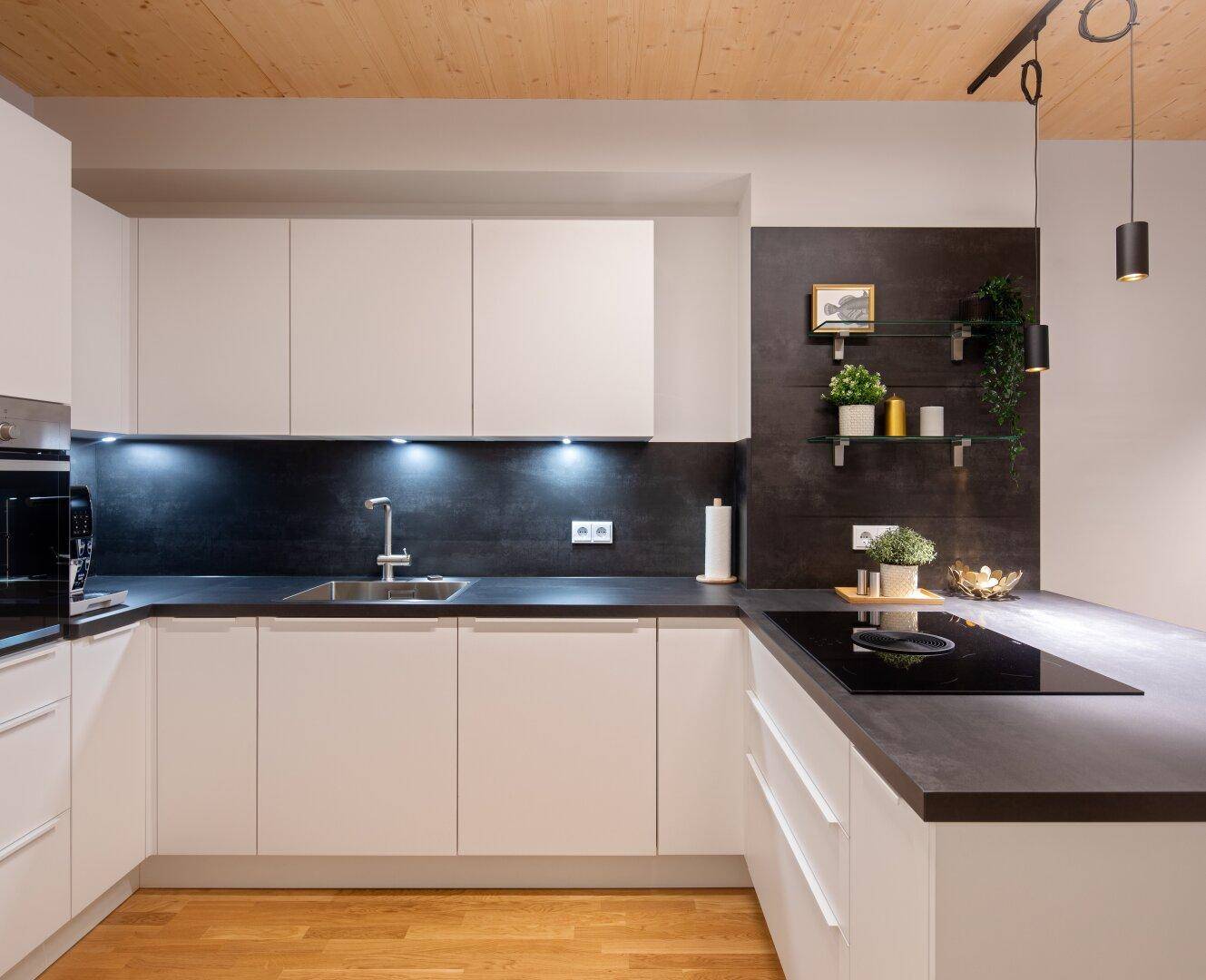 Moderne Einbauküche mit weißen Schränken, dunkler Arbeitsplatte und integrierten Geräten.