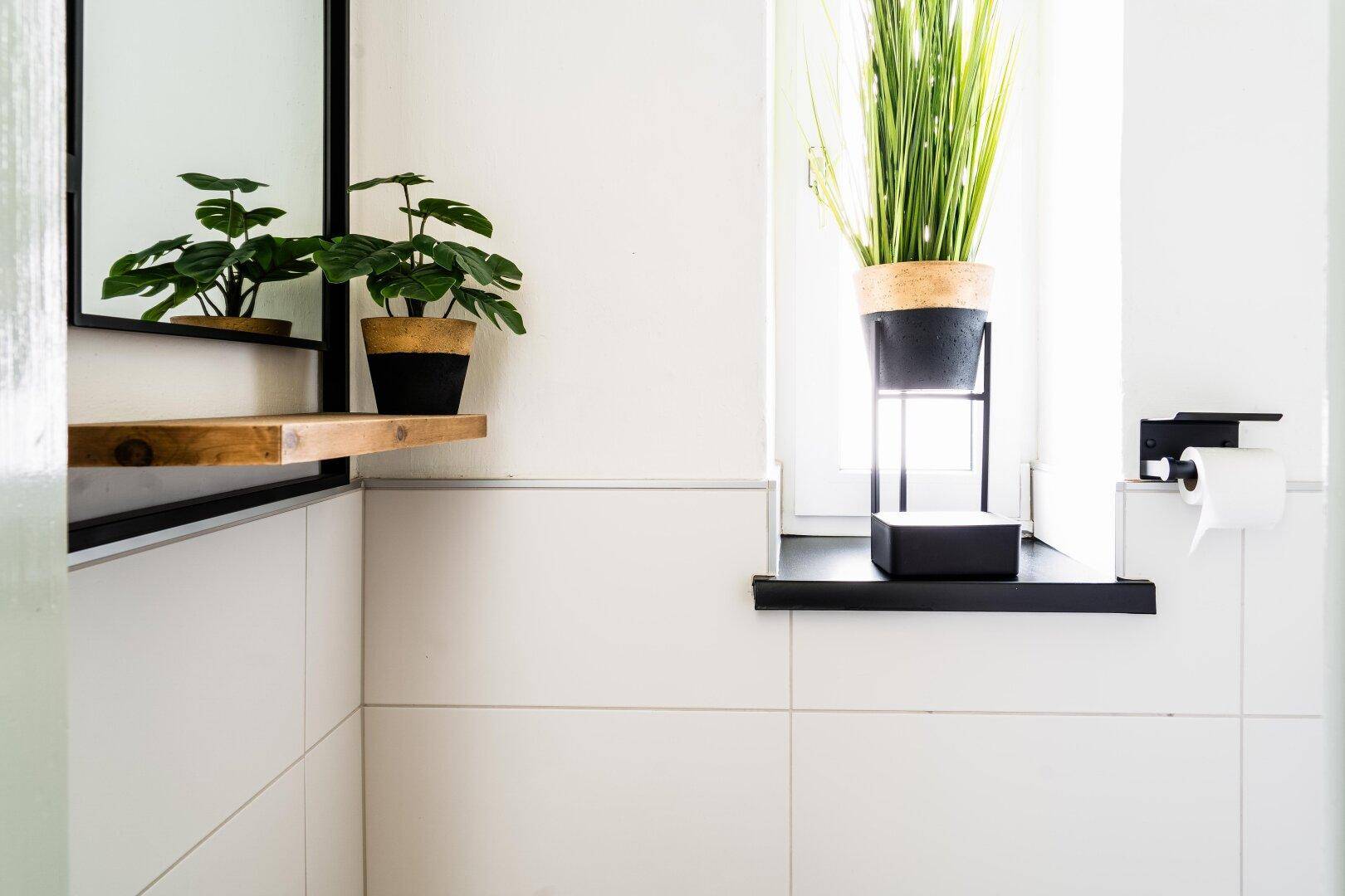 Modernes Badezimmer mit weißen Fliesen, Fenster und Pflanzen als Dekoration, minimalistisch gestaltet und hell.