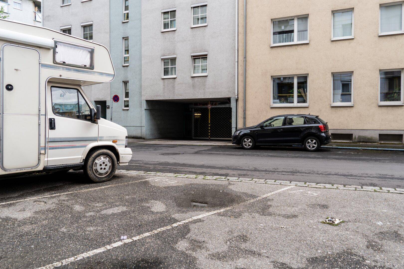 Straßenansicht mit geparktem Wohnmobil und PKW vor einem Wohngebäude mit Tiefgarageneinfahrt.