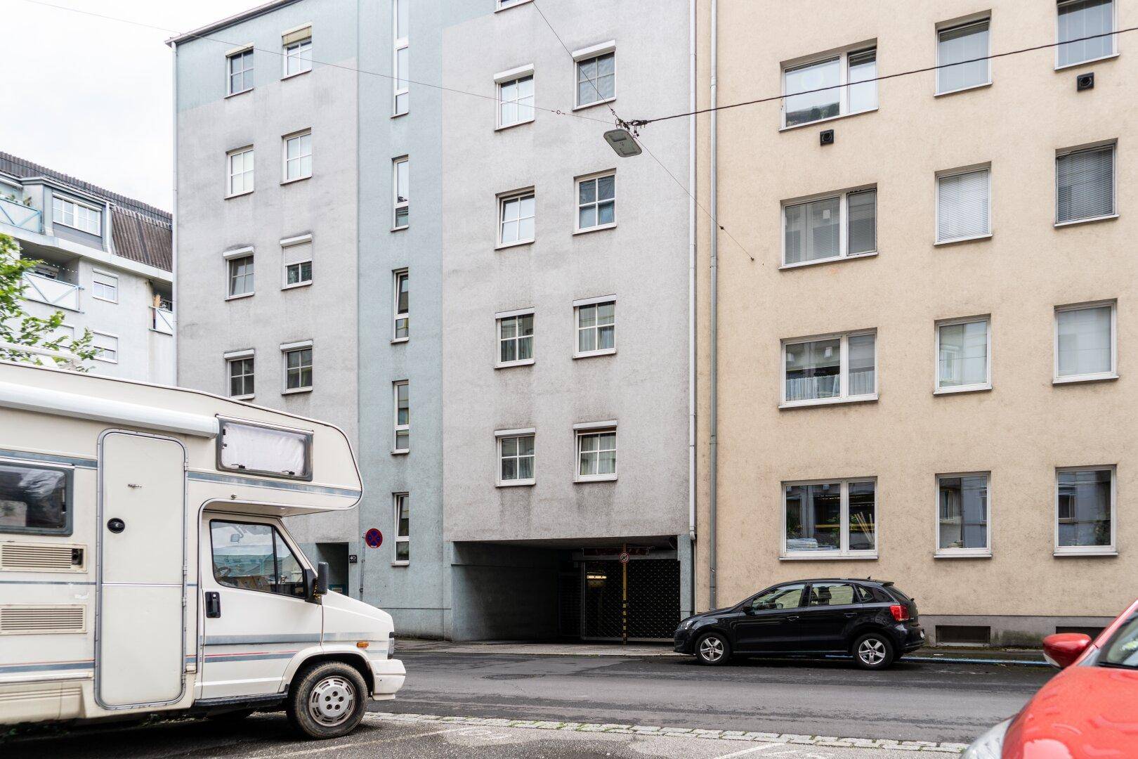 Weitläufige Straßenansicht mit Wohnmobil und PKW vor mehrstöckigen Wohngebäuden und Tiefgaragenzugang.