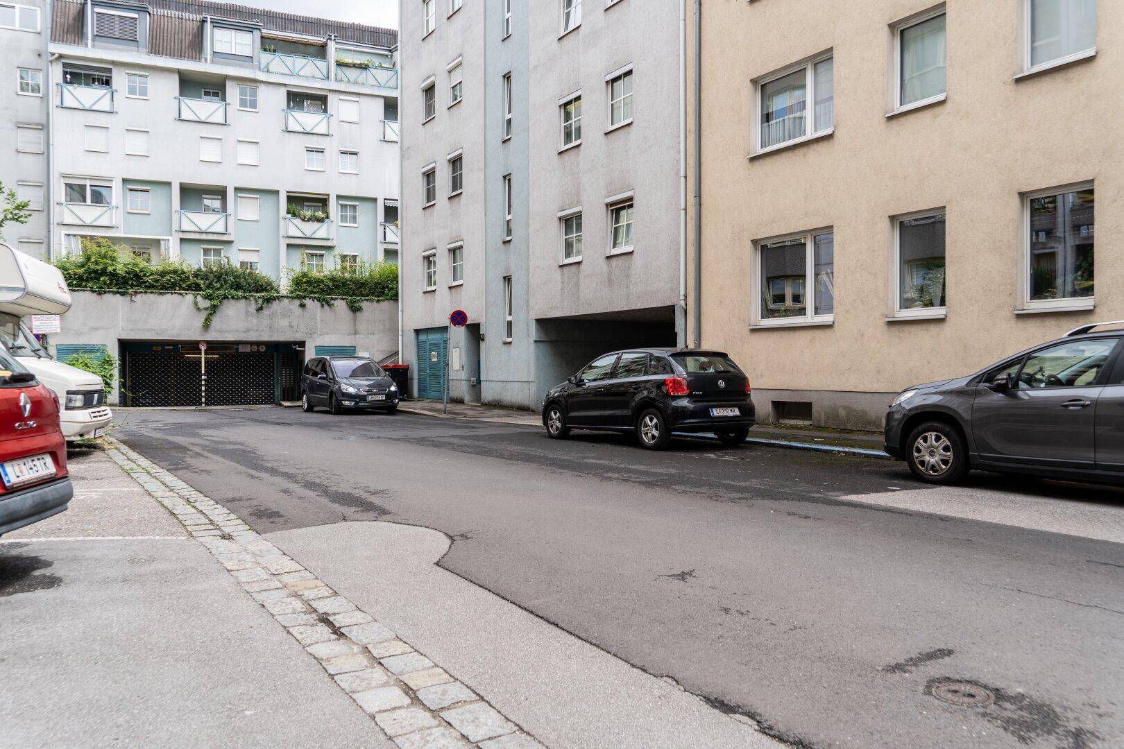 Blick entlang einer Wohnstraße mit geparkten Autos und mehreren Wohngebäuden sowie Tiefgaragenzugängen.