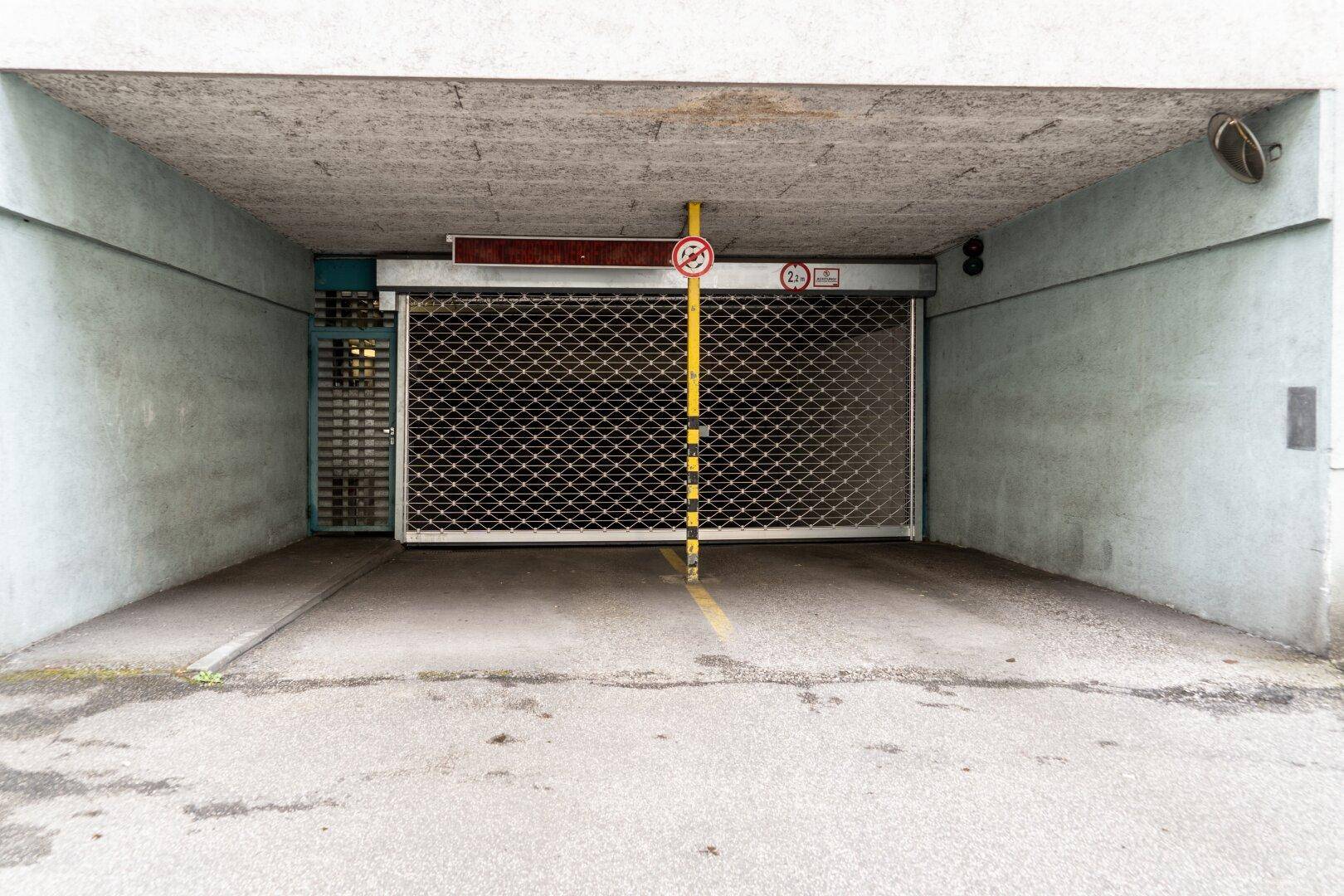 Eingang zu einer Tiefgarage mit geschlossenem Rolltor und Höhenbegrenzungsschild.